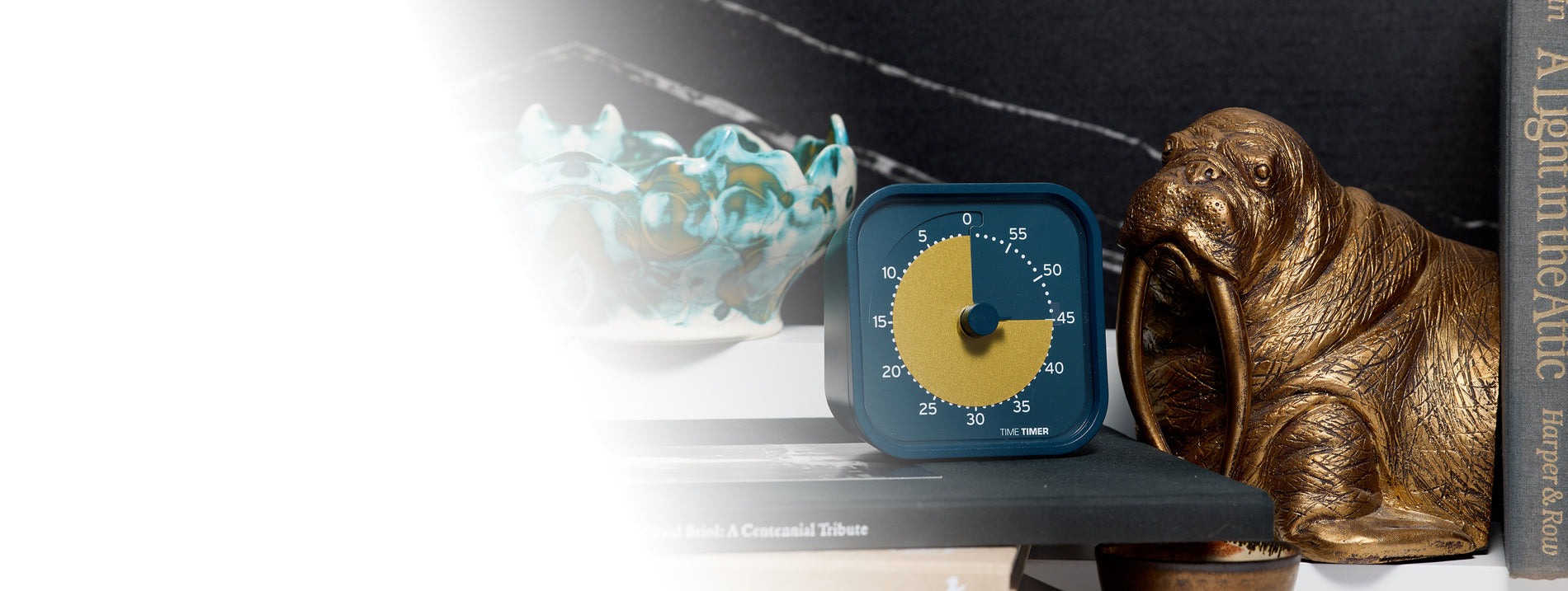Blue alarm clock with a yellow face on a shelf next to a bronze walrus figurine.