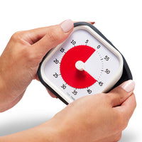 Time Timer MOD 60 Minute visual timer - the visual timer is shown being held with two hands. One hand is peeling off the silicone cover to imply it is removable. The red disk shows the visual timer is set for 45 minutes.