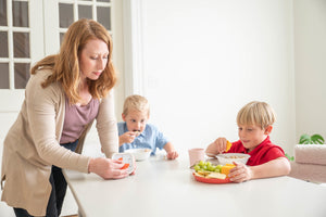 Woman and two children at a table with snacks, possibly fruits.