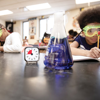 Science experiment with beaker and timer on a classroom desk