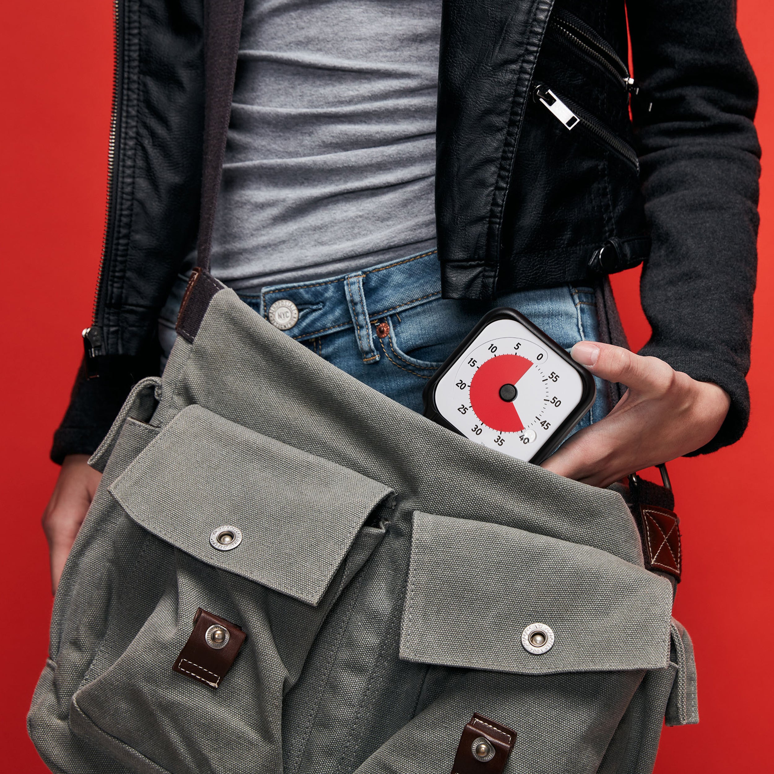 Person holding a gray bag with a digital thermometer against a red background