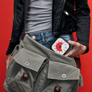 Person holding a gray bag with a digital thermometer against a red background