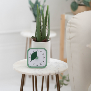 Green timer on a marble table with a potted plant in the background