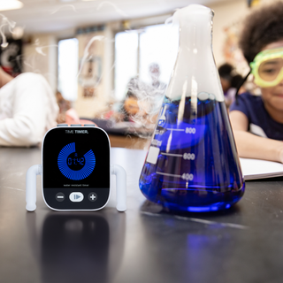 Time timer device with a beaker of blue liquid on a table in a classroom setting