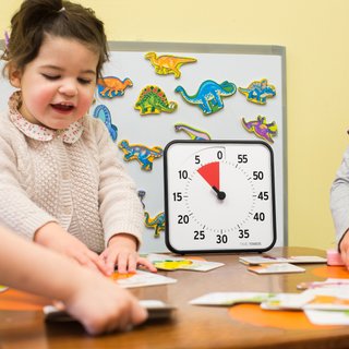 Child playing dinosaur magnets on a table and a Time Timer visual timer displaying 7 minutes. 