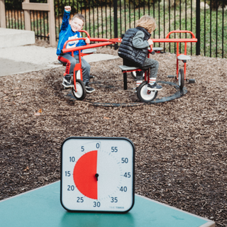 Two children playing on a red playground toy with a Time Timer visual timer in the foreground showing 30 more minutes of recess.