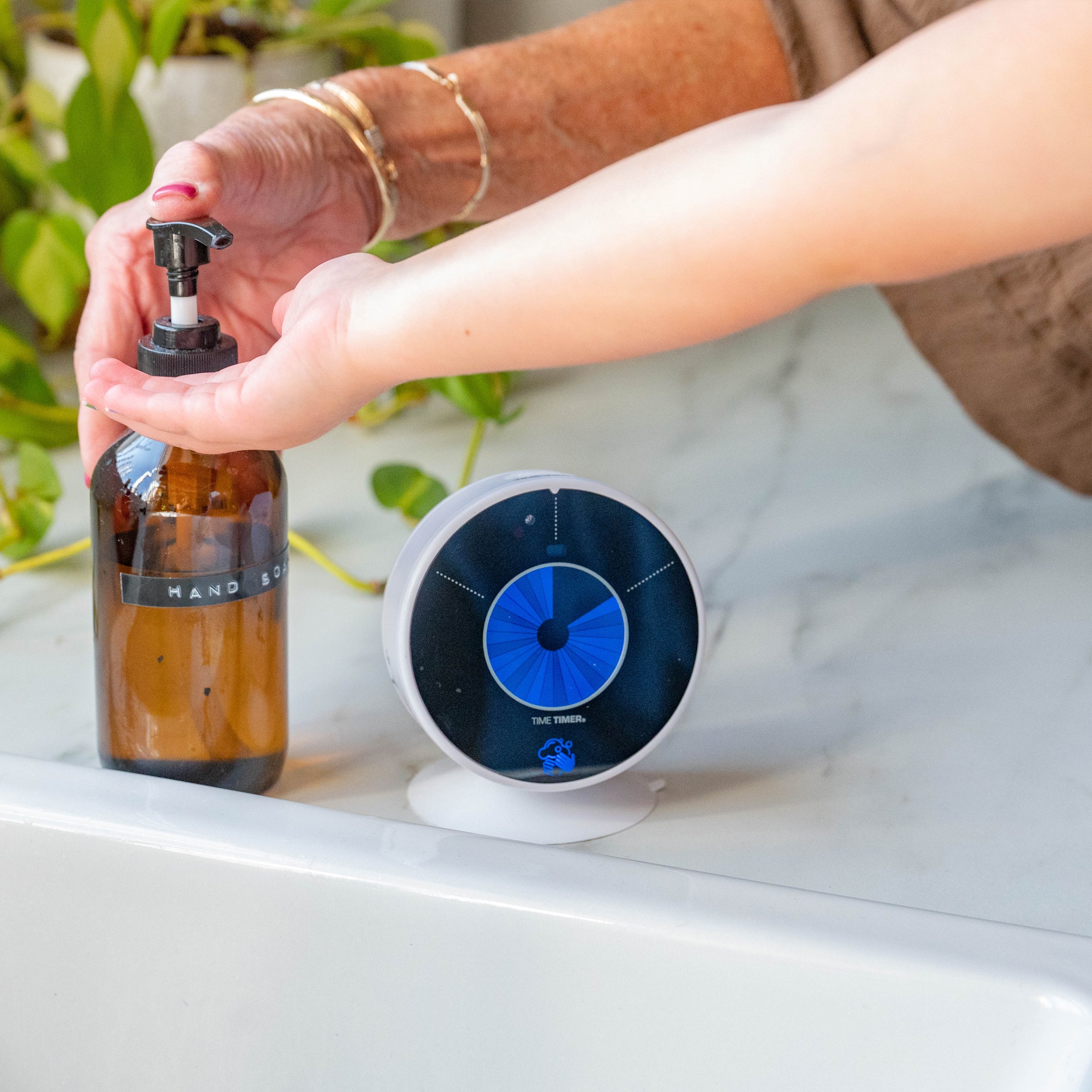 A mother or teacher helps a young toddler wash his hands at the sink by utilizing the Time Timer WASH visual timer for handwashing.