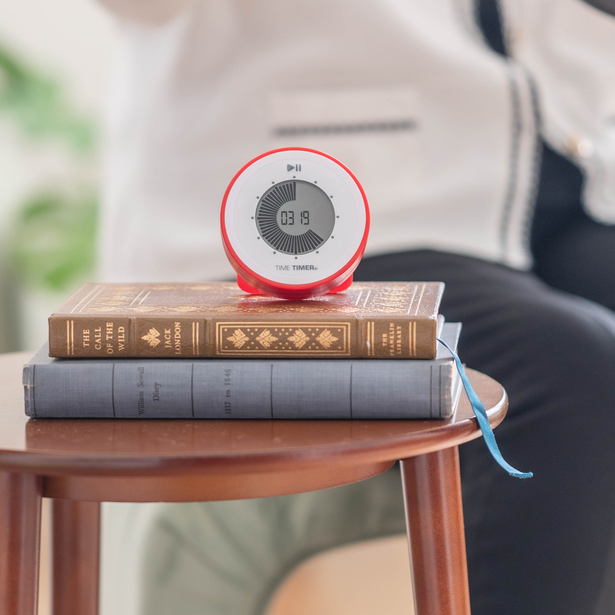 The 90-minute TWIST® Timer in Original Red sitting on two books on a side table. 