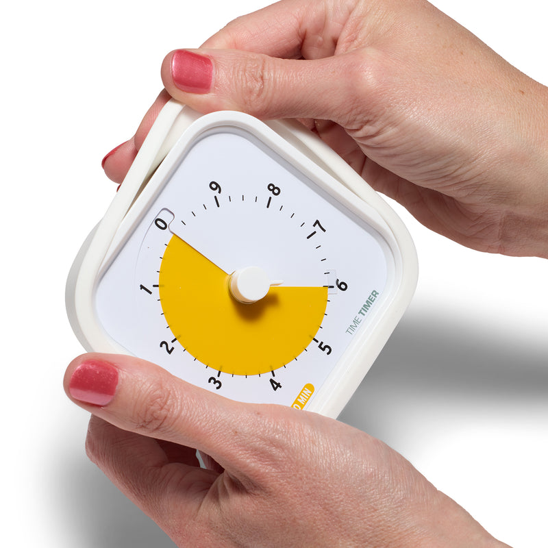 The Time Timer MOD 10 Minute Education Edition timer is being held by two hands. With one hand, the white silicone case is being peeled off of the timer.