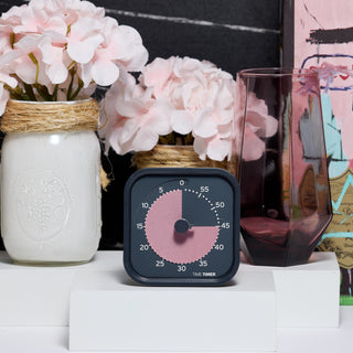 Black and pink timer on a surface with flowers and a vase in the background