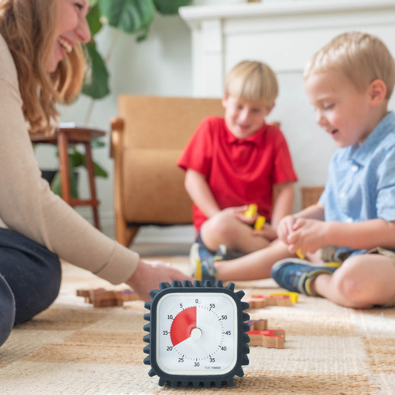 Time Timer 60-minute visual timer is on the floor in front of a mom and two kids playing. The red disk is set at 20 minutes to indicate how much time they have left to play.