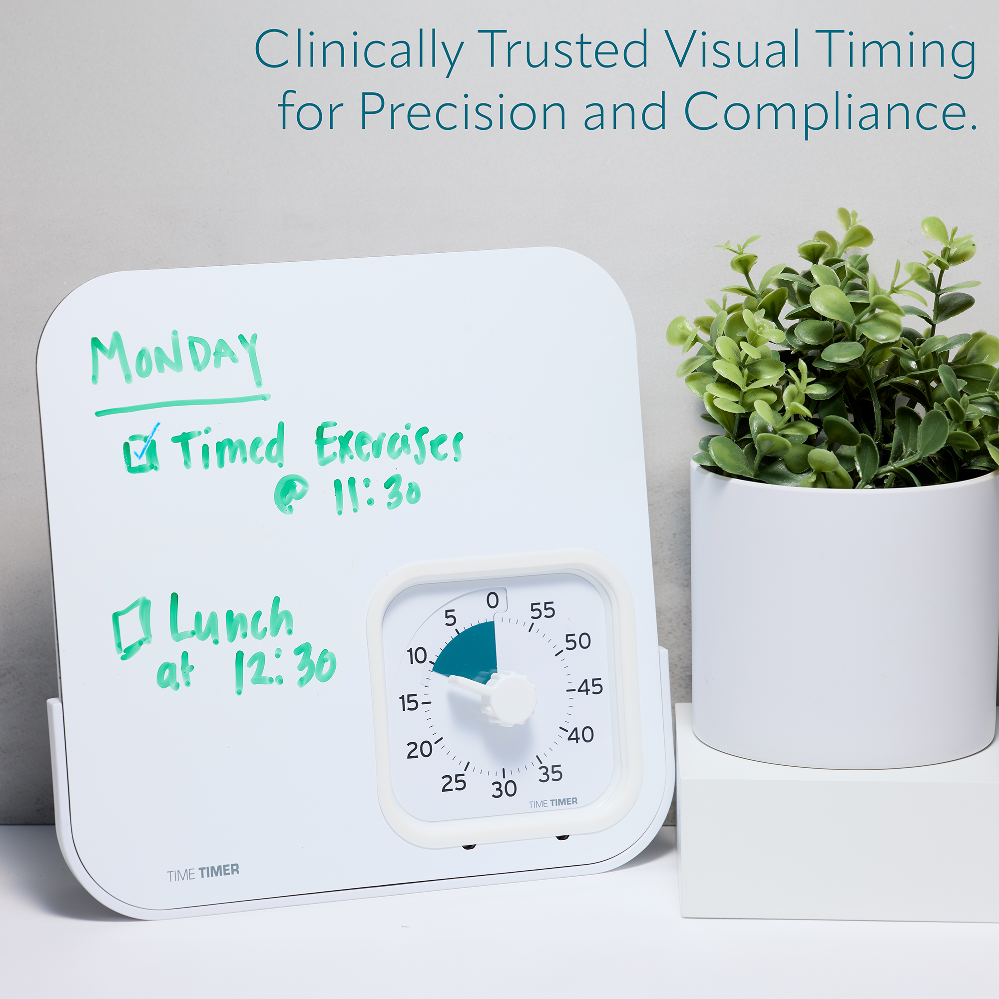 White timer with green writing next to a potted plant on a white surface.