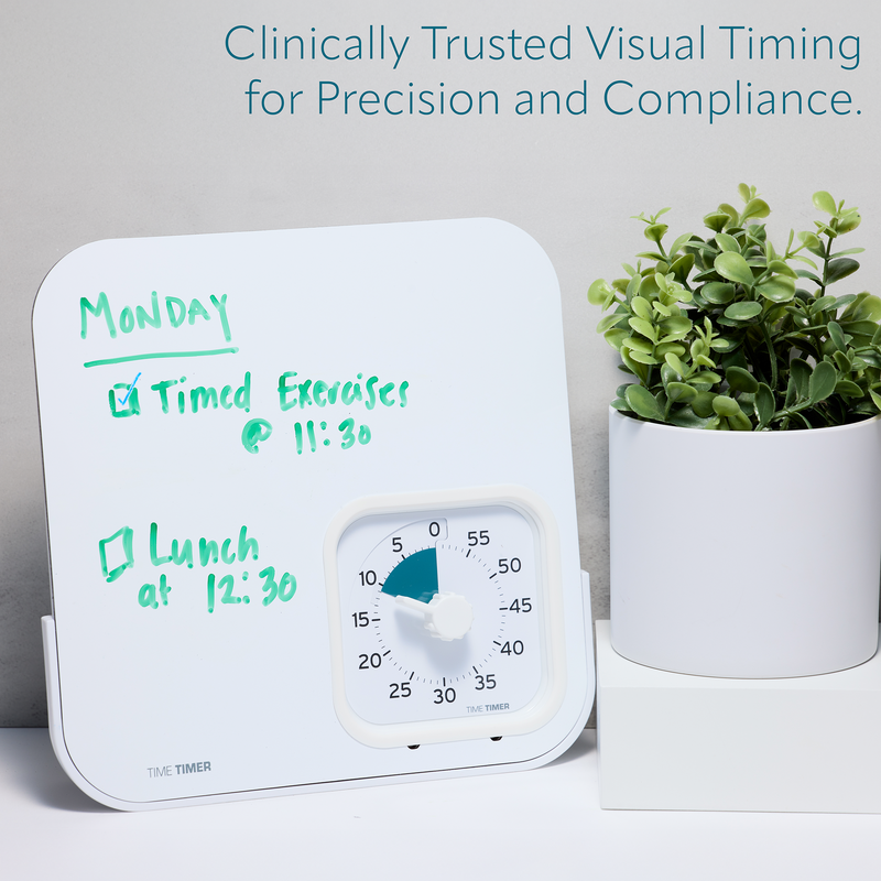 White timer with green writing next to a potted plant on a white surface.