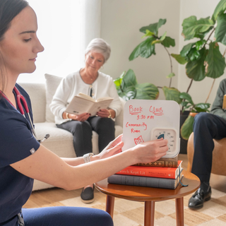 Woman holding a book club sign with others in the background in a cozy living room.