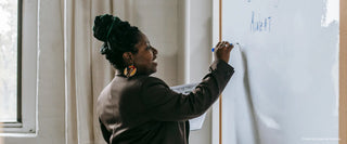 A Female black professor writing on the whiteboard.