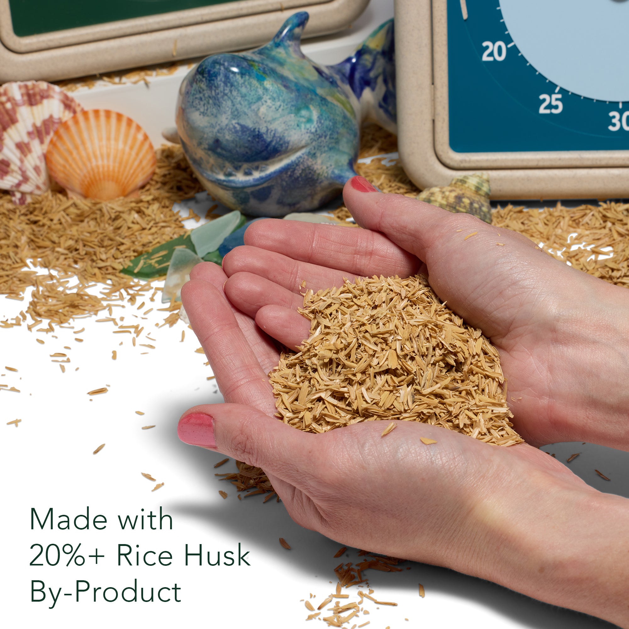 Hands are shown holding a pile of rice husks. A message is included in the photo reading "Made with 20% + Rice Husk By-Product" to indicate that the plastic used in this device is combined with rice husk material. 