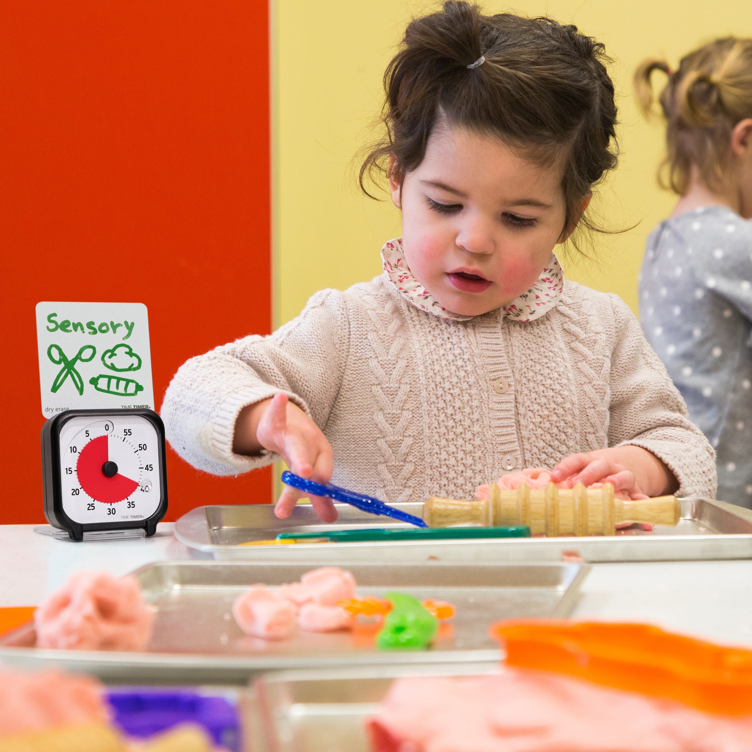 Time Timer Original 3 inch Visual Timer - Pocket. The Time Timer 3-inch is shown with the Dry Erase Activity Card. In the image, a little girl is playing at a sensory station in a preschool setting. The Timer is shown with 40 minutes on the face, and the Dry Erase card shows illustrations that communicate that she is at the Sensory Center in the classroom.