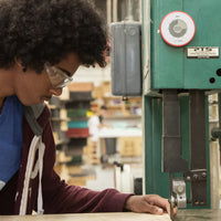 Round visual timer placed on the top of a table saw. A young man is preparing to cut a piece of wood on the table saw below the round visual timer.