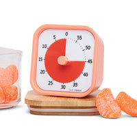 Time Timer MOD - Home Edition - visual timer. This collection of visual timers have colorful disks that disappear as time elapses. Pictured is the Dreamsicle Orange version. The outside of the timer is a sherbert colored orange while the inside is a more saturated bright orange. The timer is surrounded by orange slice candies.  