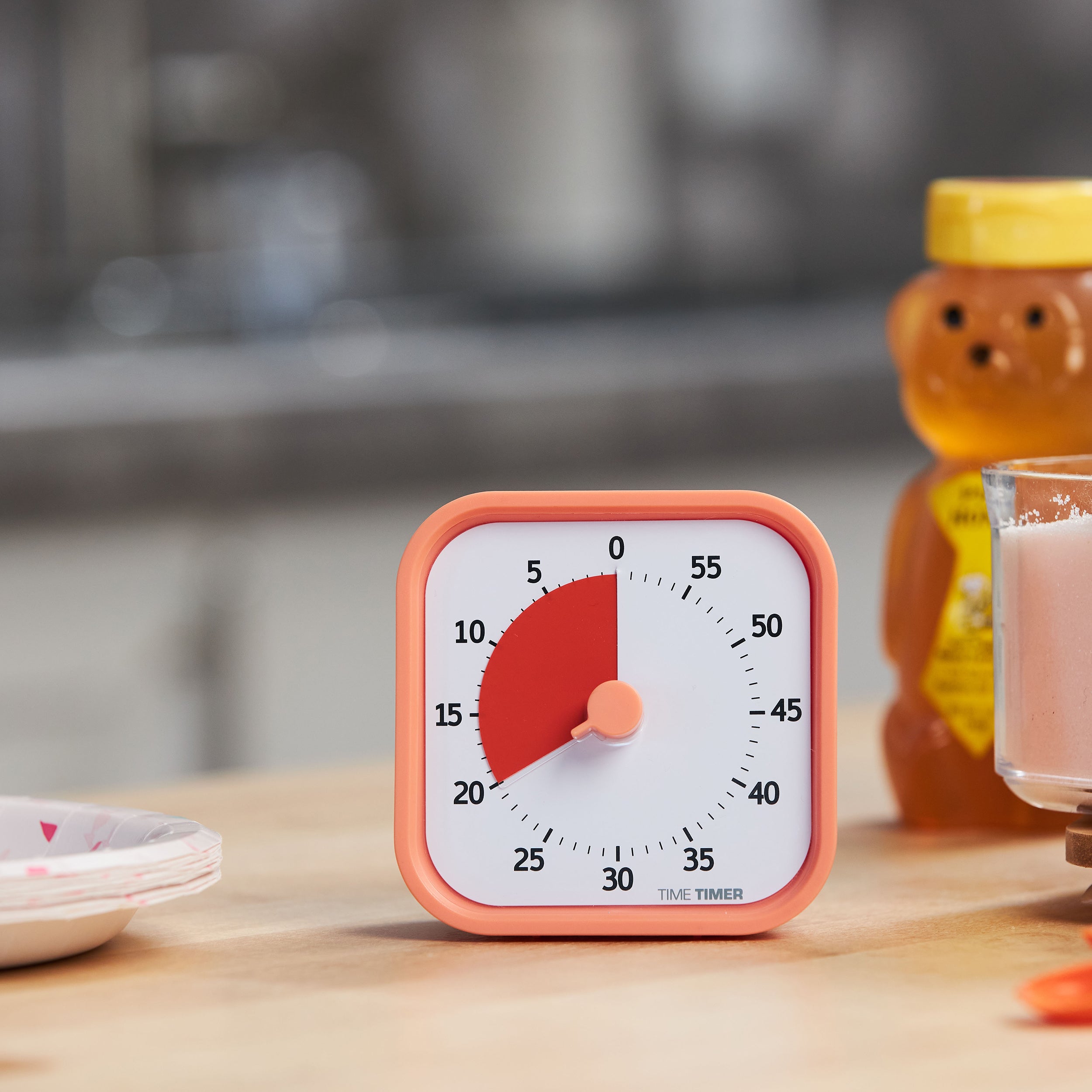 Time Timer MOD - Home Edition - This energetic visual timer is pictured on a kitchen table with a bear-shaped container of honey and some fun paper plates in the background. This is the Dreamsicle Orange color and has a sherbert colored exterior with a saturated orange colored disk that disappears as time elapses.
